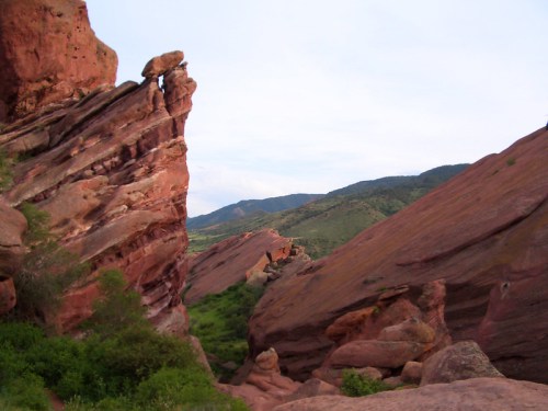 Rocky formations with red hues and green vegetation, set against a backdrop of rolling hills and a clear sky.