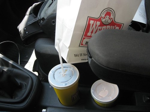 A Wendy's bag and two drinks in a car's center console.