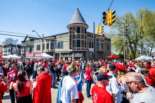 A lively street festival with a large crowd wearing red, food tents, and a historic building in the background.