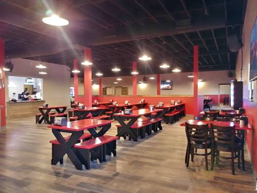 Interior of a restaurant featuring red and black tables, wooden floors, and overhead lighting.