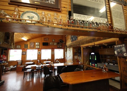 Cozy interior of a rustic bar with wooden decor, tables, and a jukebox, featuring framed pictures on the walls.