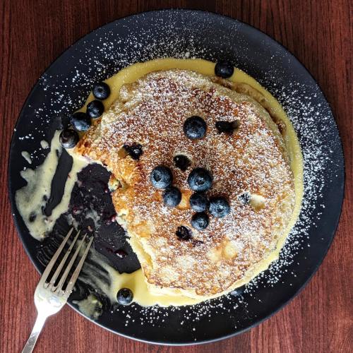 A plate of fluffy pancakes topped with blueberries and powdered sugar, drizzled with a creamy sauce.