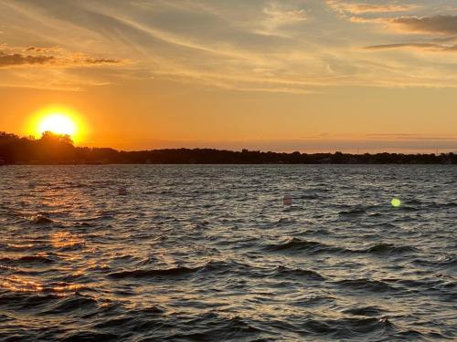 A serene sunset over a calm lake, with golden hues reflecting on the water and a silhouette of trees in the background.