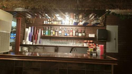 A well-stocked bar with various bottles, glasses, and a rustic wooden counter under warm lighting.