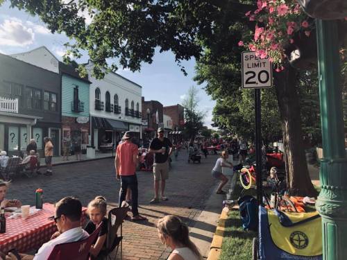 A lively street scene with people enjoying a sunny day, seated at tables, and a "Speed Limit 20" sign visible.