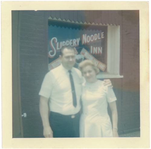 A couple stands in front of the Slippery Noodle Inn, a vintage restaurant sign visible in the background.