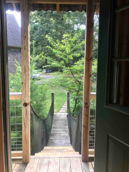 View from a doorway showing a wooden bridge leading to a lush green area with trees and a pathway.