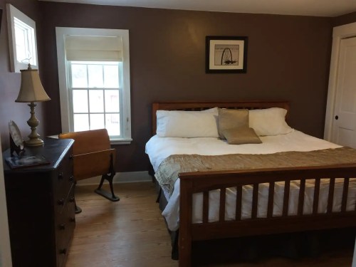 Cozy bedroom featuring a wooden bed, dresser, rocking chair, and natural light from a window.