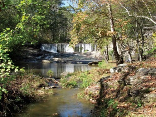 A serene landscape featuring a waterfall, calm water, and trees with autumn foliage.