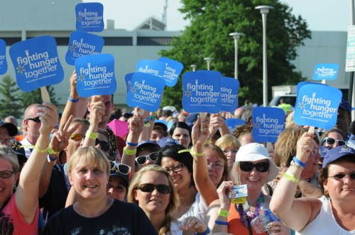 A crowd of people holding blue signs that say "fighting hunger together," showing support for a cause.