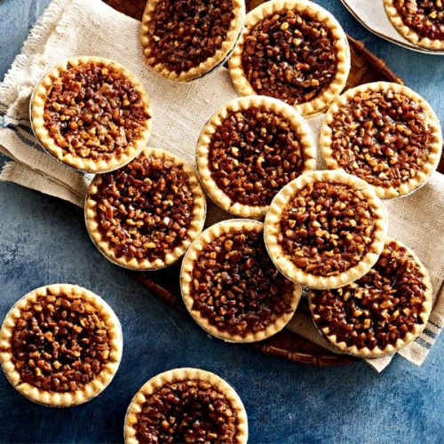 A collection of mini pecan pies arranged on a textured surface, showcasing their golden crusts and rich filling.