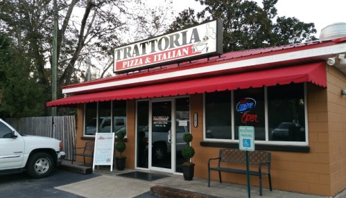 Exterior of Trattoria Pizza & Italian restaurant, featuring a red awning, sign, and outdoor seating area.