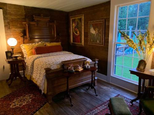 Cozy bedroom with a wooden bed, decorative pillows, artwork on the walls, and a view of the outdoors through a glass door.