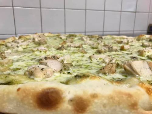 A close-up of a pizza topped with chicken and pesto sauce, featuring a golden crust and melted cheese.