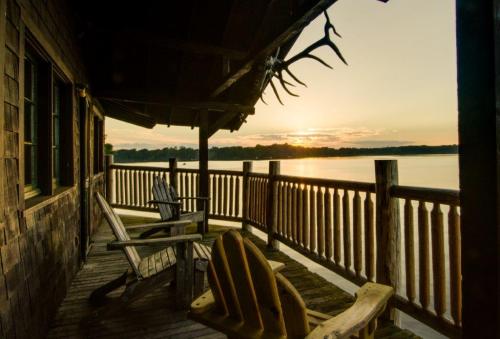 A serene lakeside view from a wooden deck with chairs, overlooking the water at sunset.