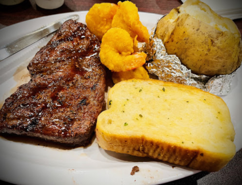 A plate with grilled steak, shrimp, a baked potato, and two slices of buttered bread.