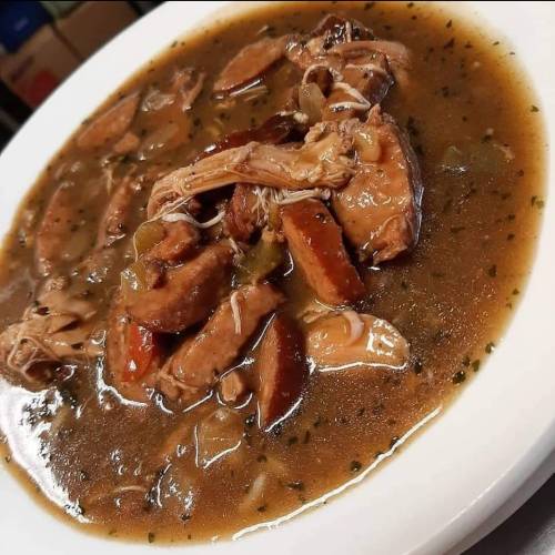 A close-up of a bowl filled with savory chicken and sausage stew, featuring vegetables in a rich, dark broth.