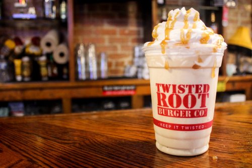 A frosty dessert drink with whipped cream and caramel drizzle, placed on a wooden table at Twisted Root Burger Co.