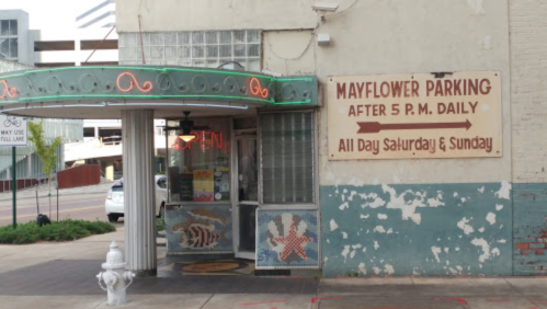 Entrance to Mayflower Parking with neon lights, a sign indicating hours, and decorative ocean-themed murals.