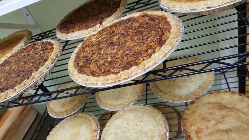 A variety of freshly baked pies cooling on a wire rack, featuring nut and fruit fillings in golden crusts.