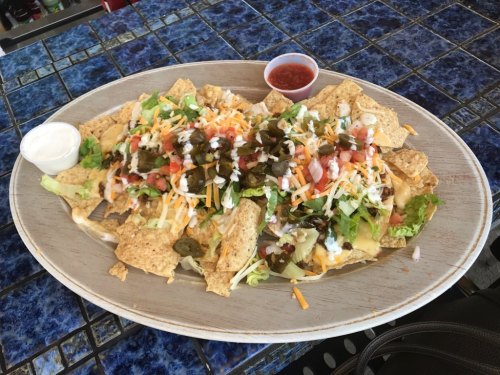 A large platter of nachos topped with cheese, lettuce, tomatoes, jalapeños, and served with salsa and sour cream.