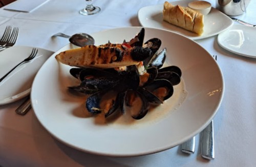 A plate of grilled seafood, including mussels and a piece of grilled fish, served with a side of bread.
