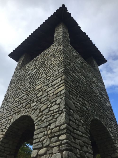 A tall stone tower with a sloped roof, viewed from below against a cloudy sky.