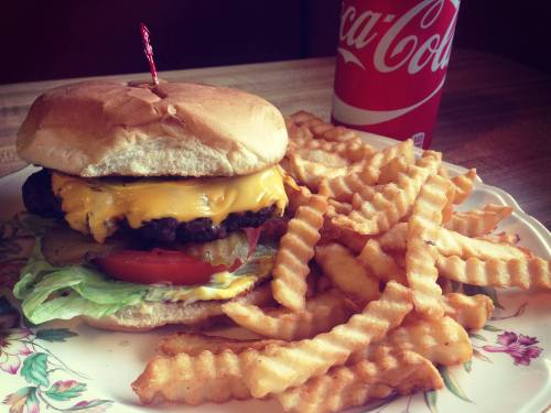 A cheeseburger with lettuce, tomato, and pickles, served with crinkle-cut fries and a can of Coca-Cola.