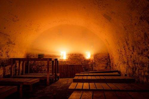 A dimly lit, arched room with wooden benches and glowing wall sconces, creating a warm, inviting atmosphere.