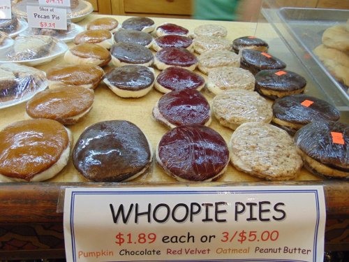 A display of various whoopie pies in plastic wrap, labeled with flavors: pumpkin, chocolate, red velvet, oatmeal, and peanut butter.
