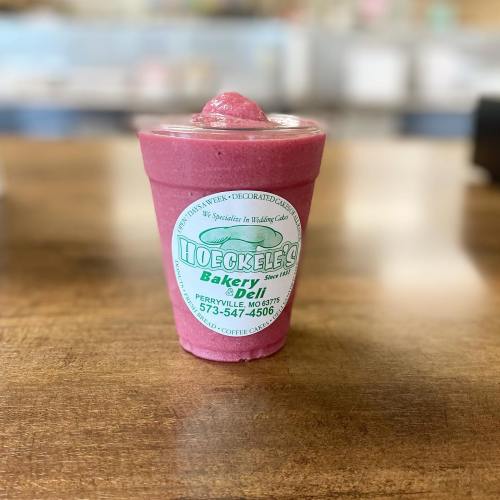 A pink smoothie in a clear cup with a logo from Hockeels Bakery & Deli, placed on a wooden table.
