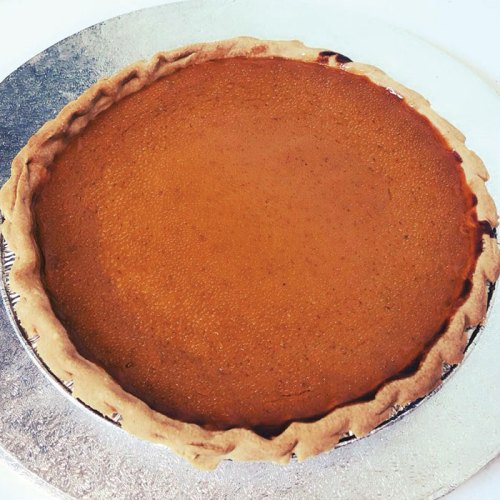 A freshly baked pumpkin pie with a golden-brown crust on a silver serving platter.