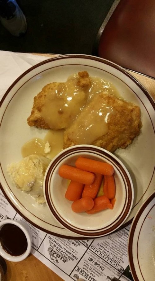 A plate of fried chicken with gravy, mashed potatoes, and a side of steamed carrots.