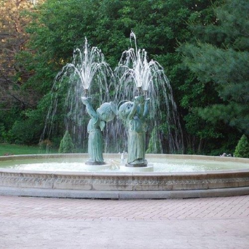 Two cherubic statues in a fountain, joyfully spraying water, surrounded by lush greenery.