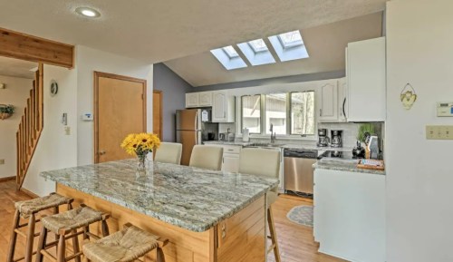 Bright kitchen with skylights, granite island, white cabinets, and wooden floors, featuring a vase of sunflowers.