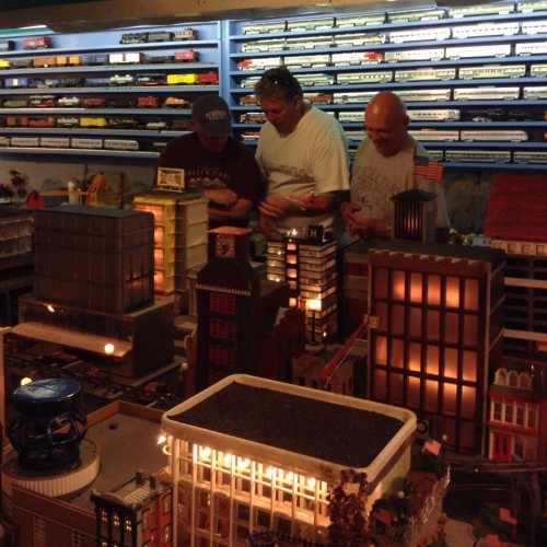 Three people interact with a detailed model city, featuring illuminated buildings and a variety of miniature structures.