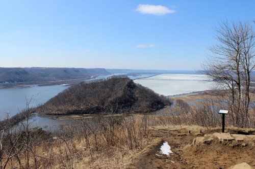 A scenic view of a river winding through hills, with a clear blue sky and sparse trees in the foreground.