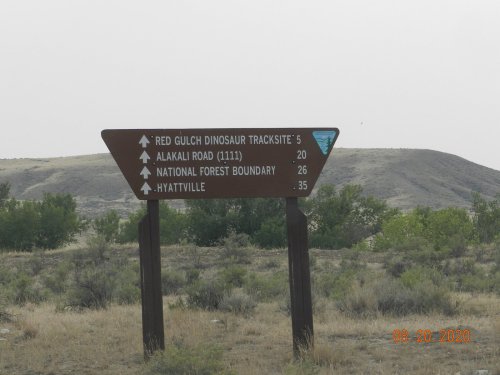 Signpost indicating directions and distances to Red Gulch Dinosaur Tracksite, Alkali Road, National Forest Boundary, and Hyattville.