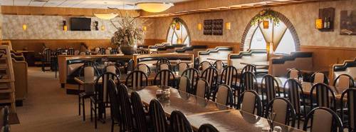 Interior of a spacious restaurant with wooden decor, arched windows, and rows of black chairs and tables.