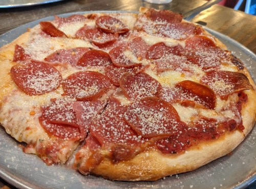 A close-up of a pepperoni pizza topped with cheese and grated Parmesan on a metal plate.