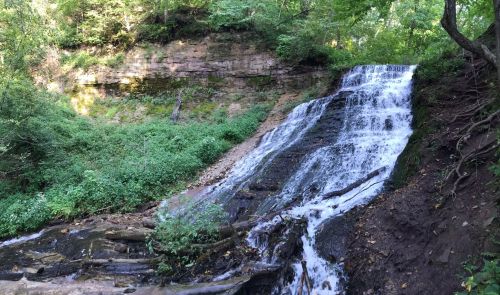 A serene waterfall cascading over rocky terrain, surrounded by lush greenery and steep cliffs.