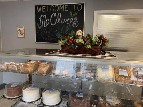 A display case with various baked goods and a festive holiday decoration in a bakery. A chalkboard welcomes visitors.