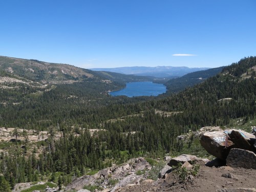 A scenic view of a lake surrounded by mountains and dense forests under a clear blue sky.