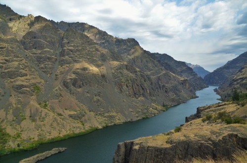 A winding river flows through rugged mountains under a cloudy sky, showcasing a serene natural landscape.