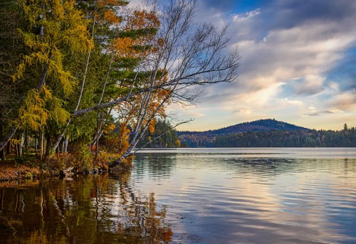 A serene lake scene with autumn foliage, reflecting trees and clouds under a colorful sky.