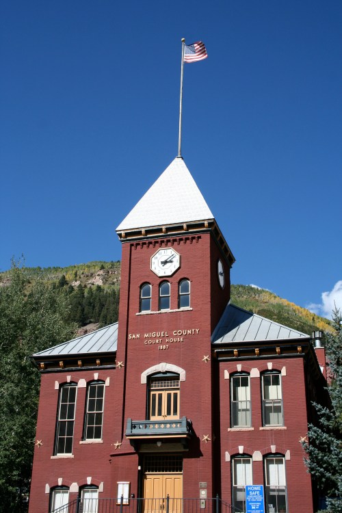 Historic red brick courthouse with a clock tower and American flag against a clear blue sky.