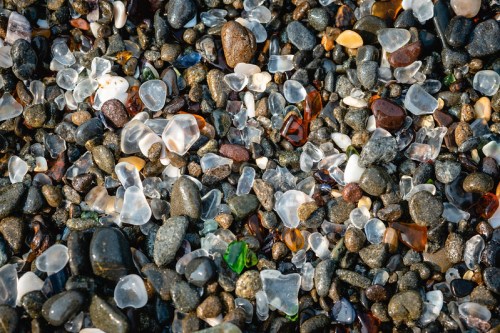A close-up of a pebbly beach covered in colorful sea glass and smooth stones.