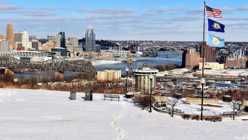 Snow-covered landscape with a view of a city skyline, river, and flags waving in the foreground.