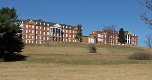 Historic brick buildings on a grassy hillside under a clear blue sky.