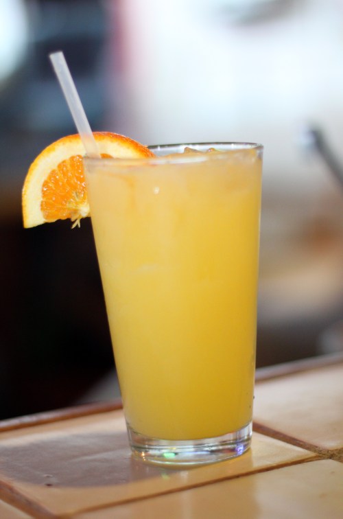 A refreshing orange drink with ice, garnished with a slice of orange and served in a tall glass with a straw.